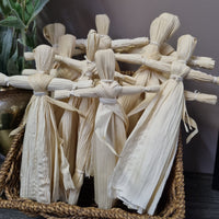 A basket containing handmade beige corn dolls, also known as effigy dolls, made from organic corn husks and bound with cotton.
