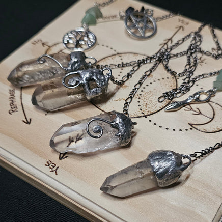 Several clear crystal point pendant necklaces with silver-toned chains and caps are arranged on a light wood display board against a dark background.