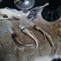 A collection of handmade wands with deer antler and crystal points, displayed on a faux fur surface. The wands have various metallic pigment clay coatings and waxed cord wraps, with spaces for adding charms or feathers.