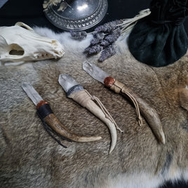 A collection of handmade wands with deer antler and crystal points, displayed on a faux fur surface. The wands have various metallic pigment clay coatings and waxed cord wraps, with spaces for adding charms or feathers.